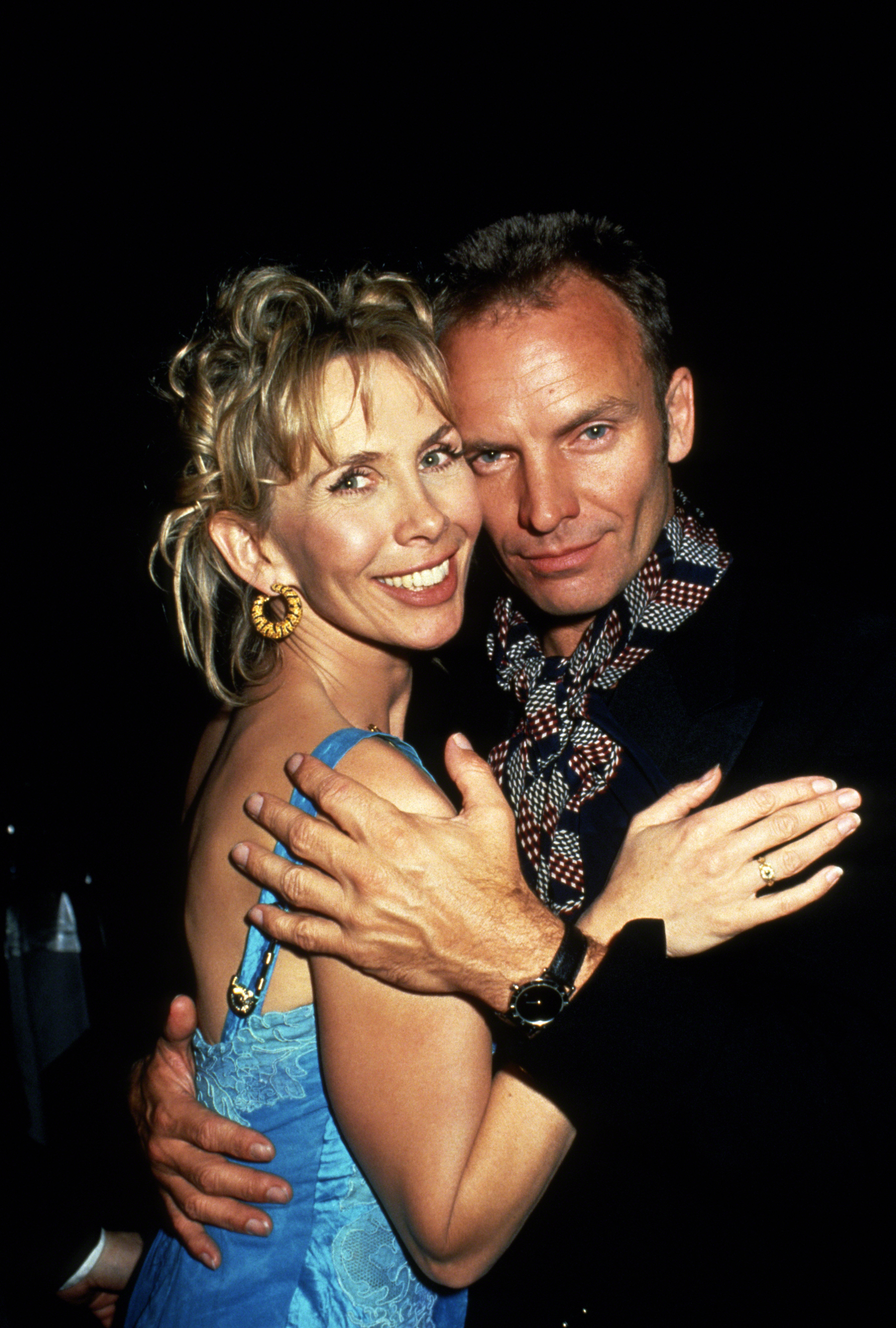 Trudie Styler wears a bright blue, thin-strapped dress and large, round gold earrings as she smiles while hugging Sting, circa 1994, in New York City.