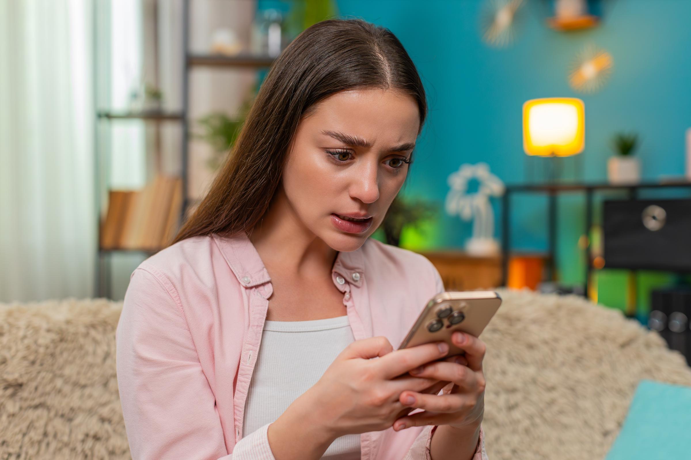 A young woman sitting on home sofa angrily types on her smartphone. | Source: Getty Images