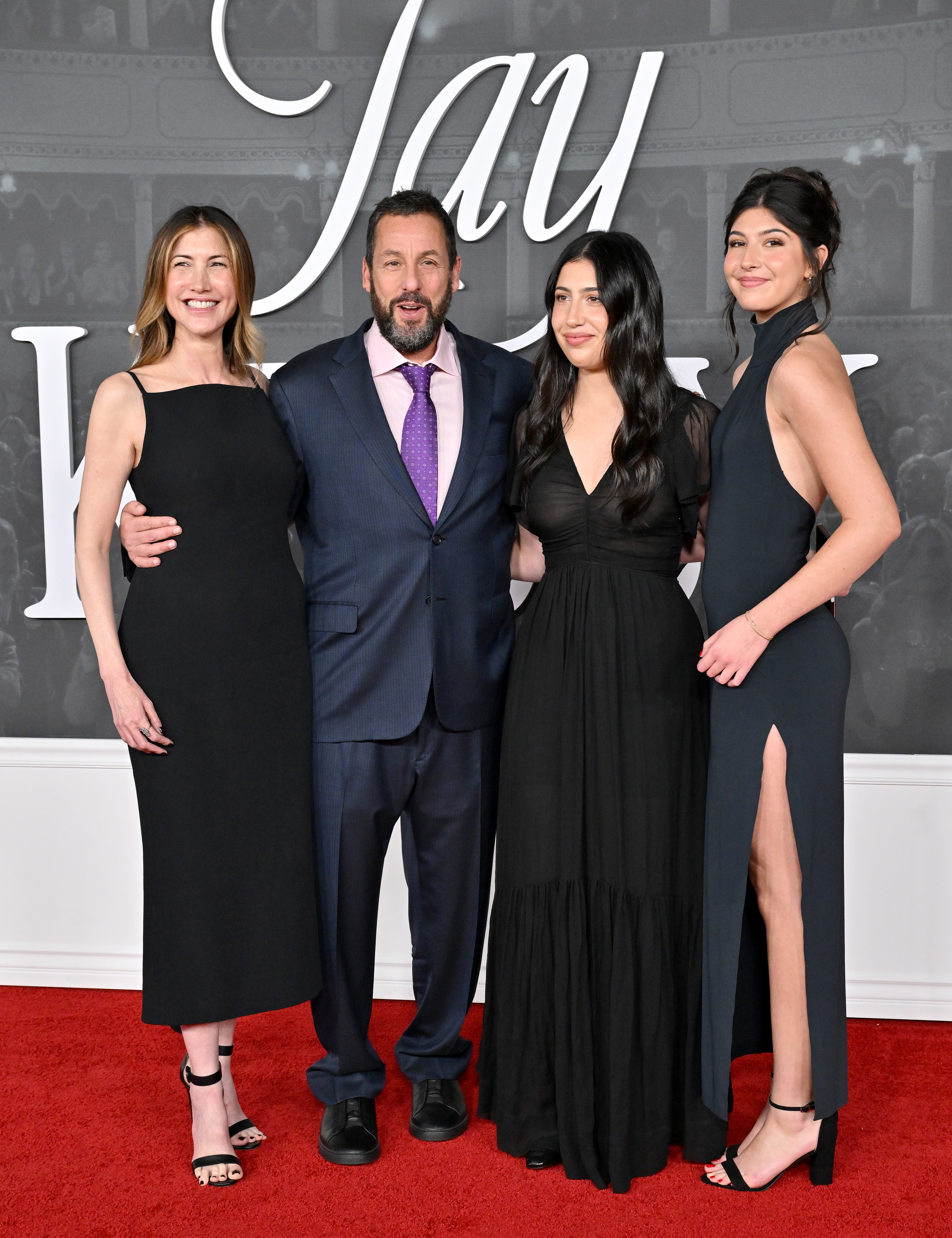 Adam Sandler, flanked by Jackie and his daughters Sadie and Sunny, appears caught mid-conversation in this shot. Their excitement and energy are palpable through their body language as they attend the "Jay Kelly" premiere.
