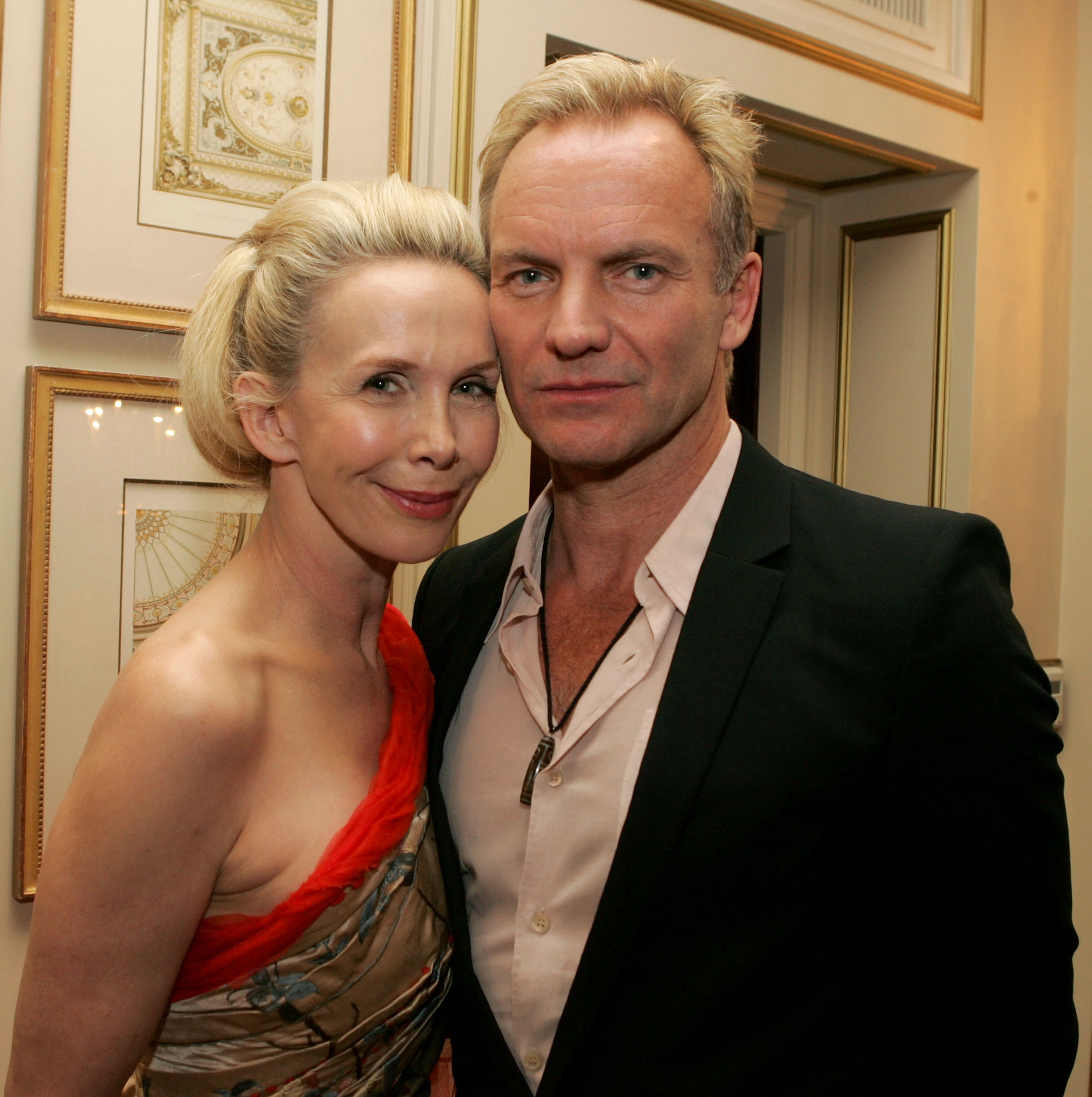 Trudie Styler wears a strapless gown featuring a gold patterned fabric with a draped coral-red sash detail, while arriving with Sting at the first annual UNICEF Snowflake Ball at the Regent Beverly Wilshire Hotel on November 30, 2005, in Beverly Hills, California.