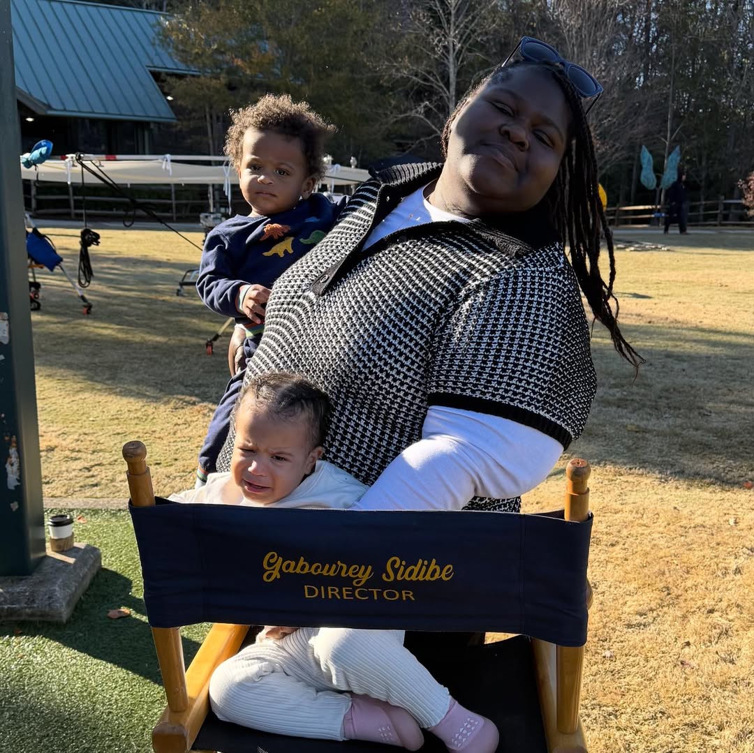 Facing the camera, Gabourey Sidibe stands slightly turned with Cooper in her arm and Maya seated in the chair. She smiles softly as Maya looks off to the side, mid-expression. | Source: Instagram/brandontour