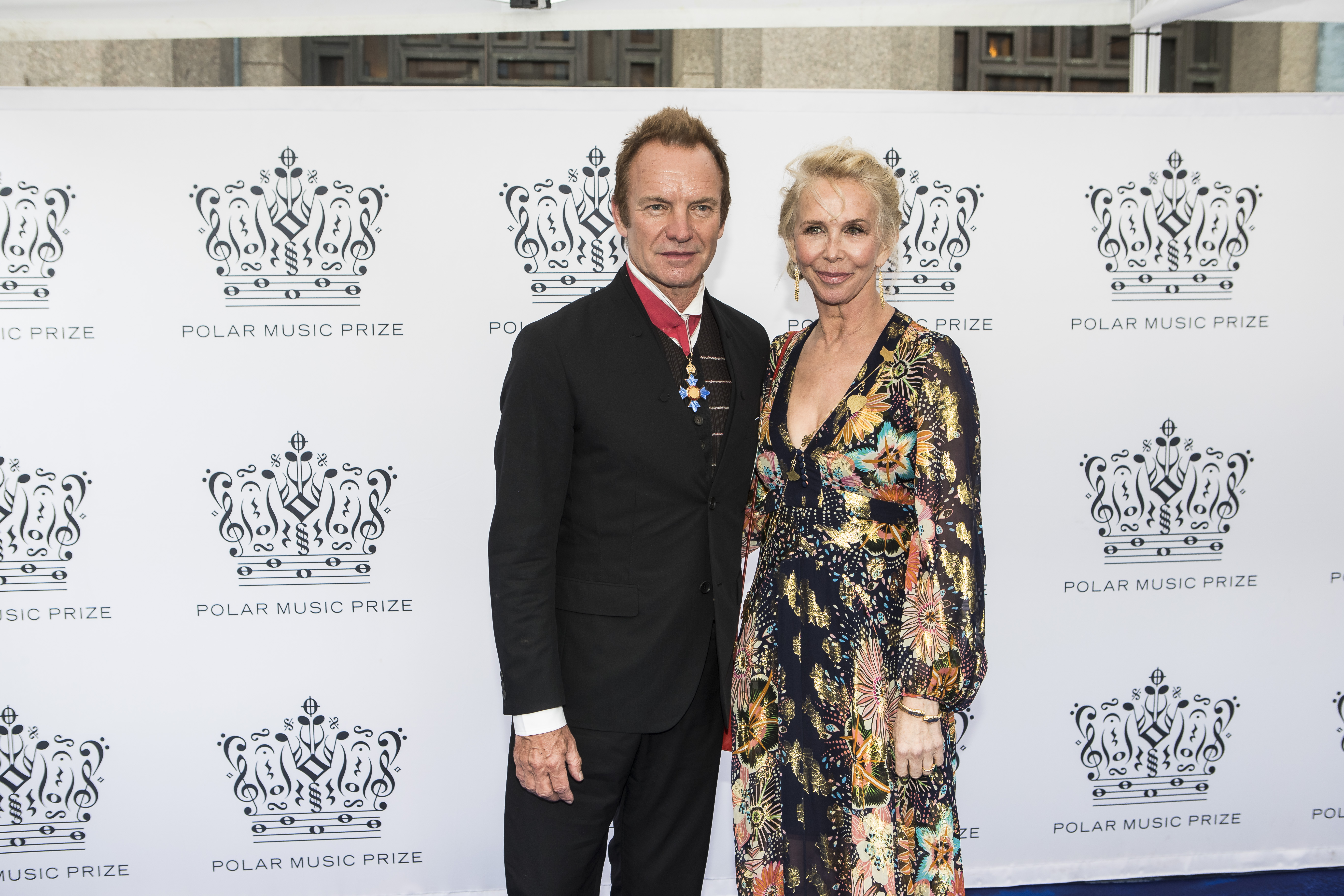 Trudie Styler wears a long-sleeved, deep v-neck gown with a dark floral and nature-inspired pattern in shades of orange, yellow, and blue, while attending the Polar Music Prize with Sting on June 15, 2017, in Stockholm, Sweden.