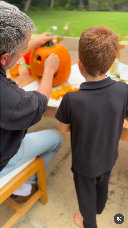 Archie stands beside an adult as the adult carves a large pumpkin, as seen in the post dated October 26, 2025 | Source: Instagram/meghan