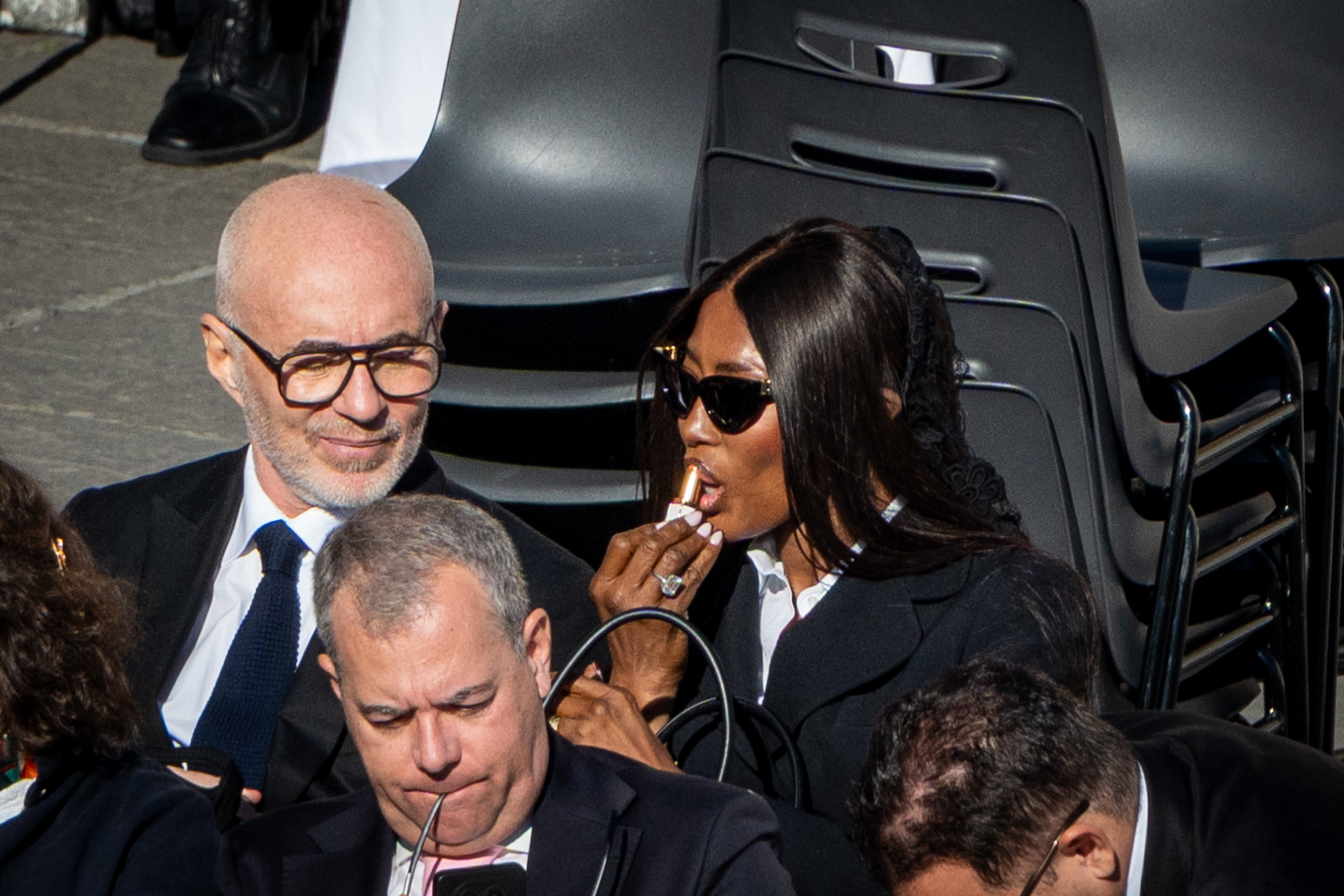 Naomi Campbell applying lipstick as she sits in the audience. | Source: Getty Images